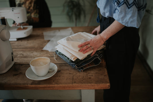 hands moving a stack of fabric on a wooden table next to a cup of coffee