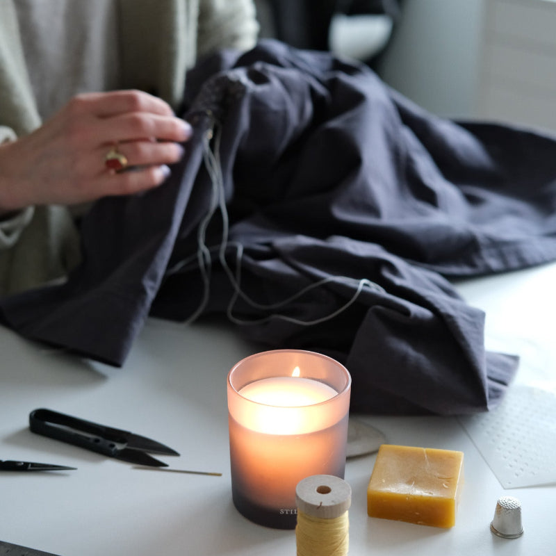 Person working on a sewing project with a candle and tools on a table.