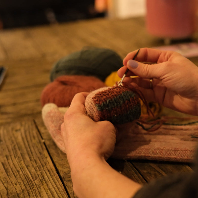 Close-up of hands knitting with yarn on a wooden surface.