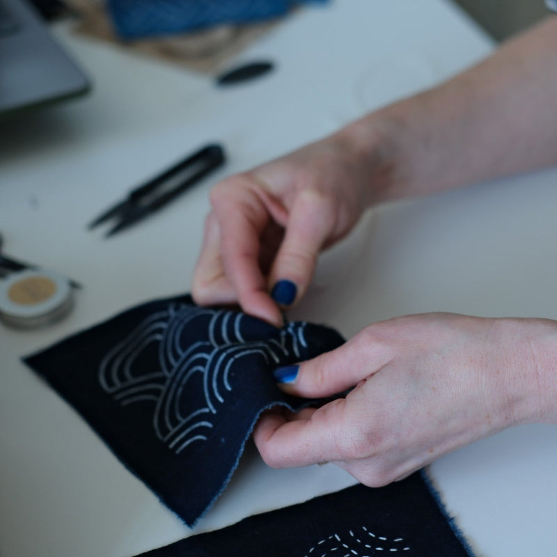 Person working on a sashiko project with fabric and sewing tools on a table.
