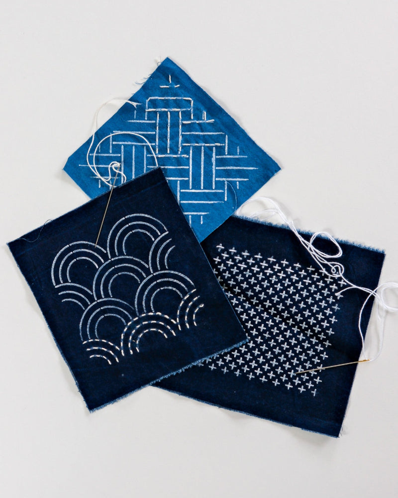 Three blue fabric samples with white embroidery patterns on a light gray background