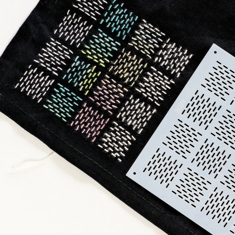 Two black and white sashiko stencils on a black fabric background