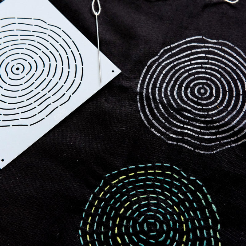 Black fabric with circular embroidered sashiko patterns and a white template on a black background
