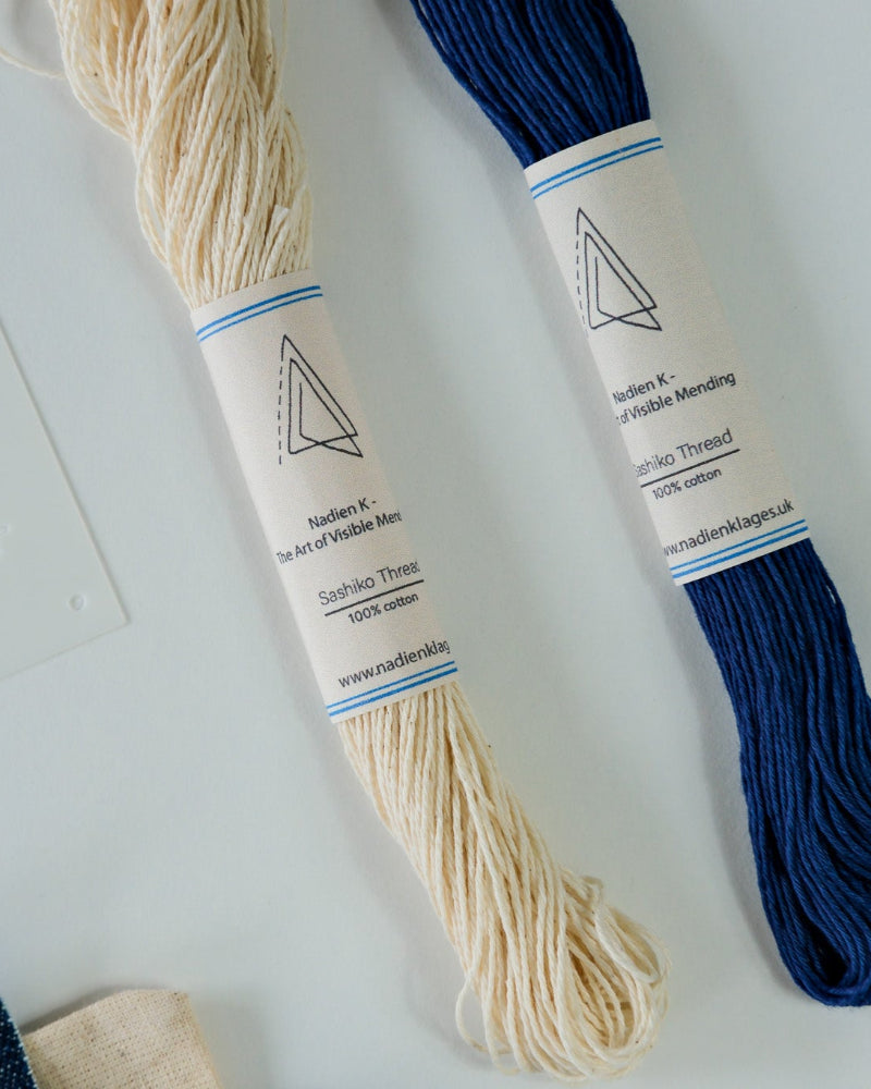 Two skeins of sashiko thread, one white and one blue, on a textured surface.