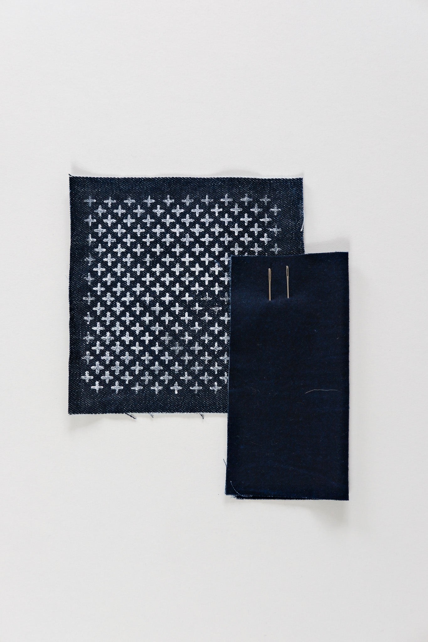 Classic cross-stitch Sashiko pattern in chalk on an indigo swatch with two needles