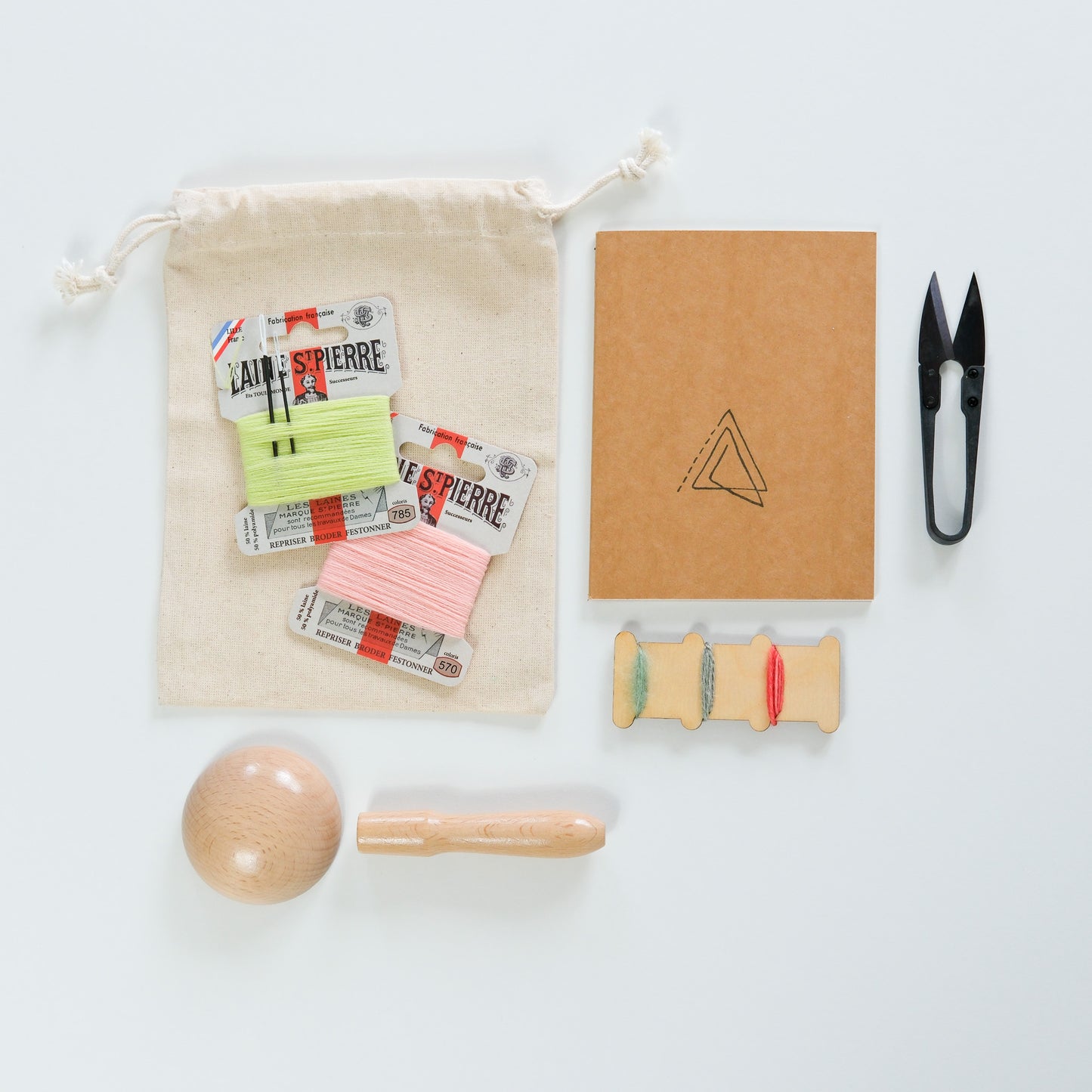 Collection of stationery items including a notebook, a variety of threads, and a darning mushroom on a white background.