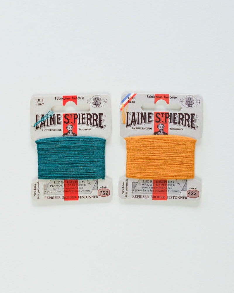 Two packages of Laine Spierre yarn, one petrol and one orange, on a white background.