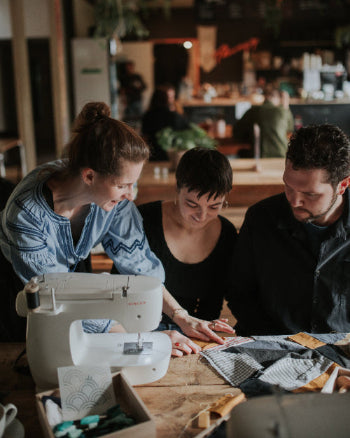 Three people working on a sewing project with a sewing machine in a workshop setting.