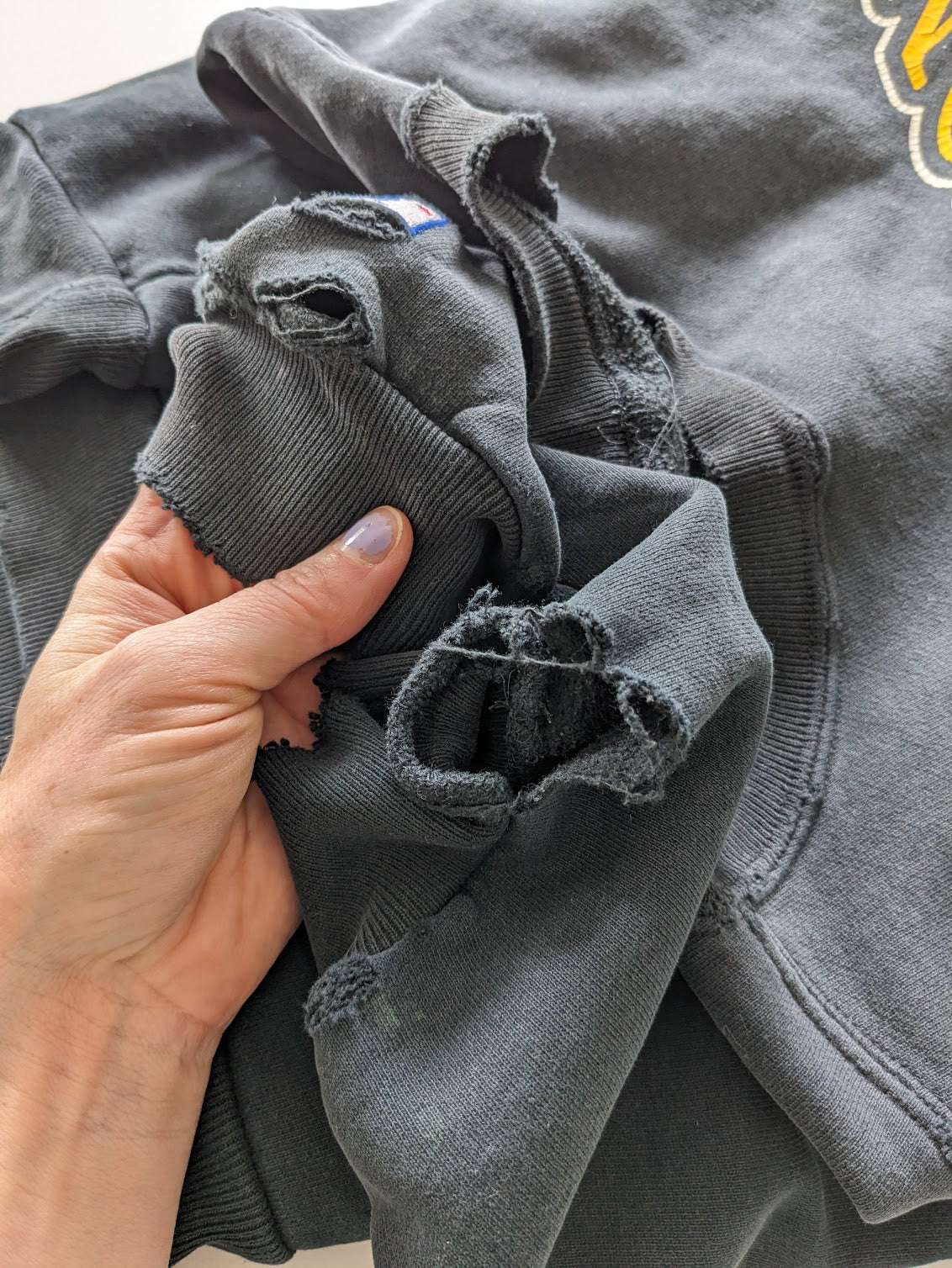 Gray distressed hoodie held by a hand with visible wear and tear.