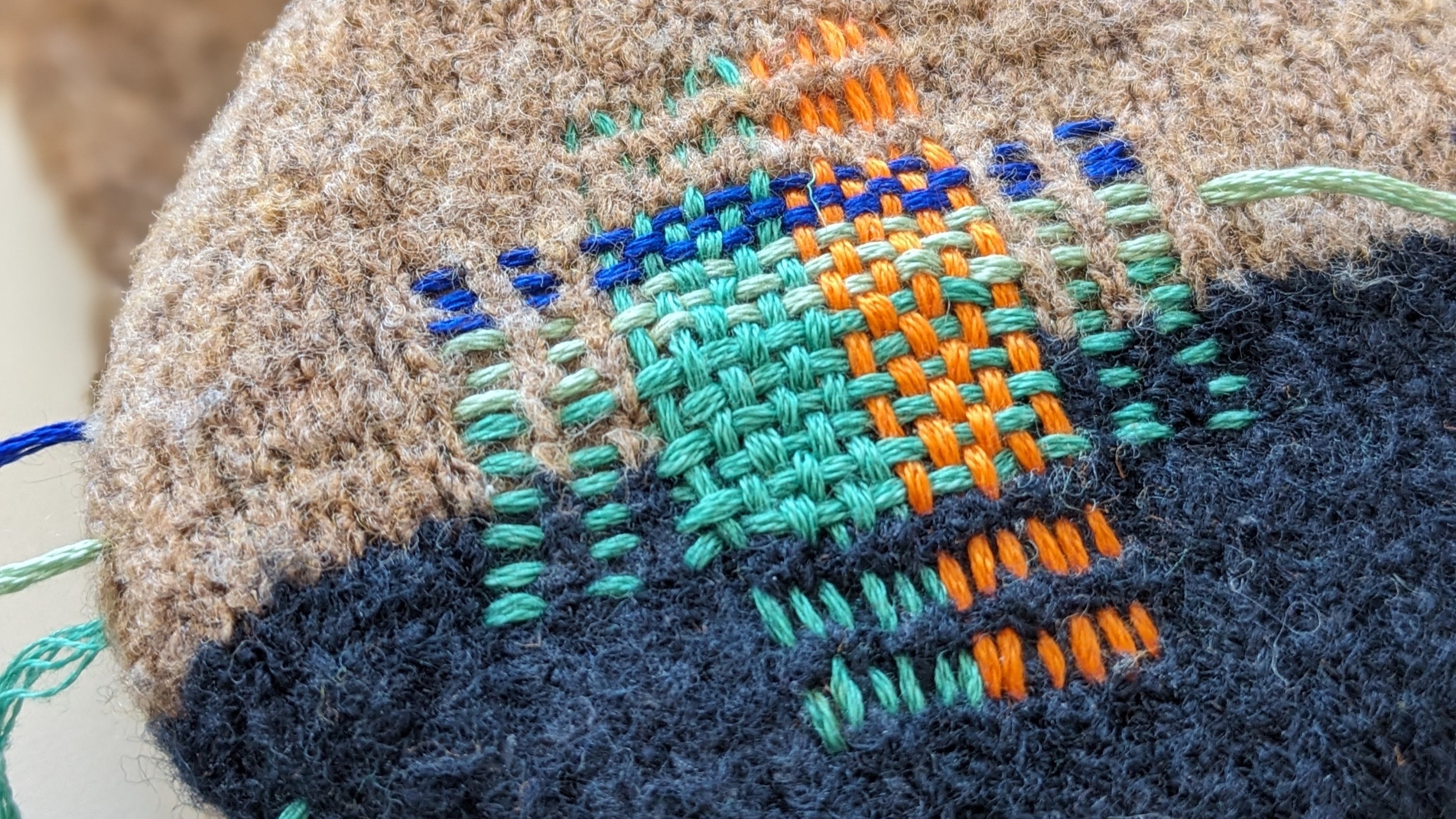 Textile art piece with cross-stitch design on a fabric ball.
