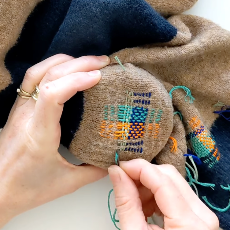 Person stitching a small embroidered item on a piece of fabric.