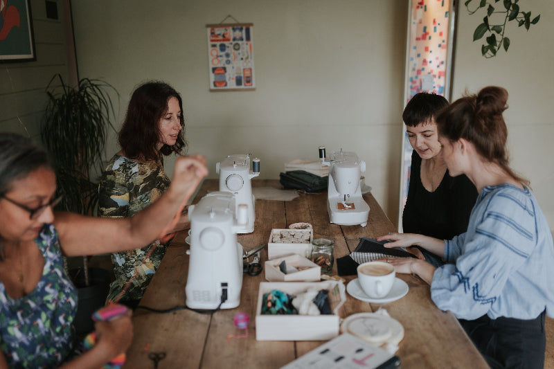 Group of women working together at a table with various items and sewing equipment.