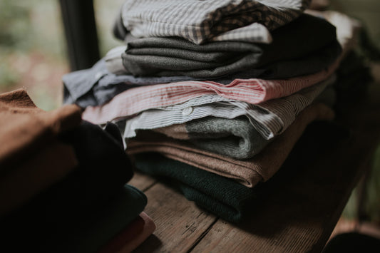 Pile of shirts and jumpers on wooden table waiting to be mended.