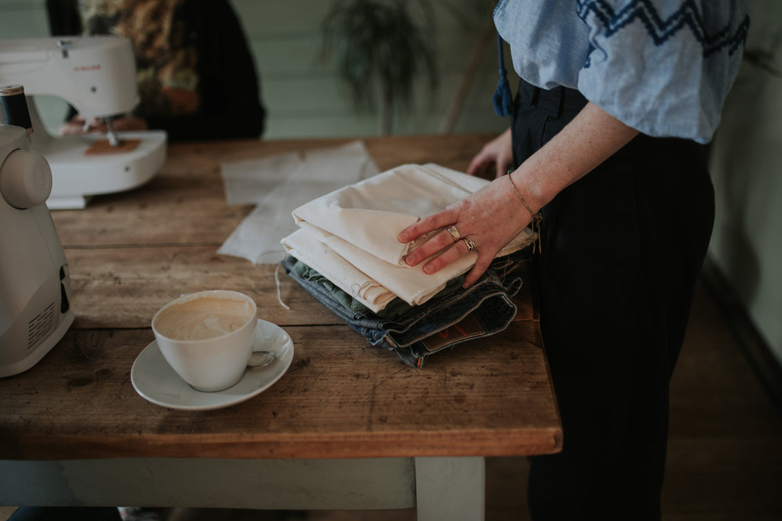 hands moving a stack of fabric on a wooden table next to a cup of coffee
