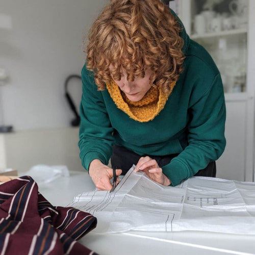 Person cutting fabric with scissors at a table in a private sewing and uypcycling workshop setting