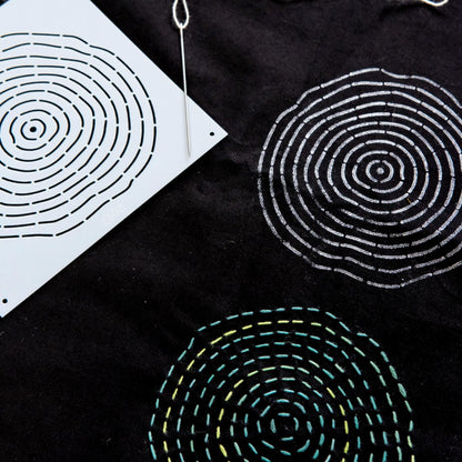 Black fabric with circular embroidered sashiko patterns and a white template on a black background