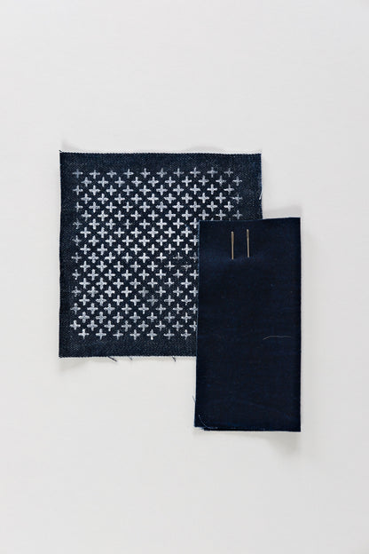 Classic cross-stitch Sashiko pattern in chalk on an indigo swatch with two needles