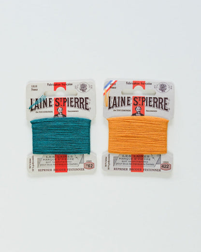Two packages of Laine Spierre yarn, one petrol and one orange, on a white background.
