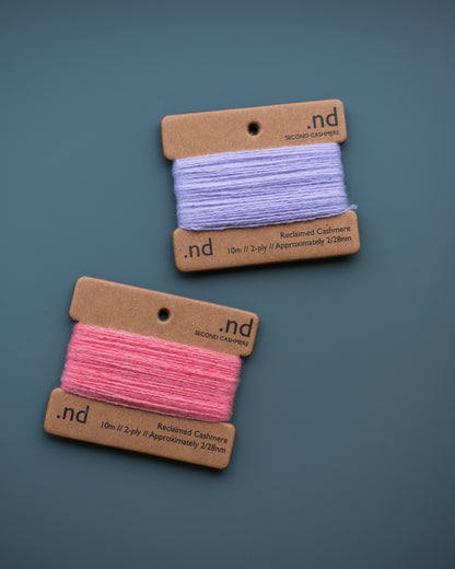 Two spools of cashmere thread, one pink and one purple, on brown cardboard labels with 'nd' branding against a blue background.