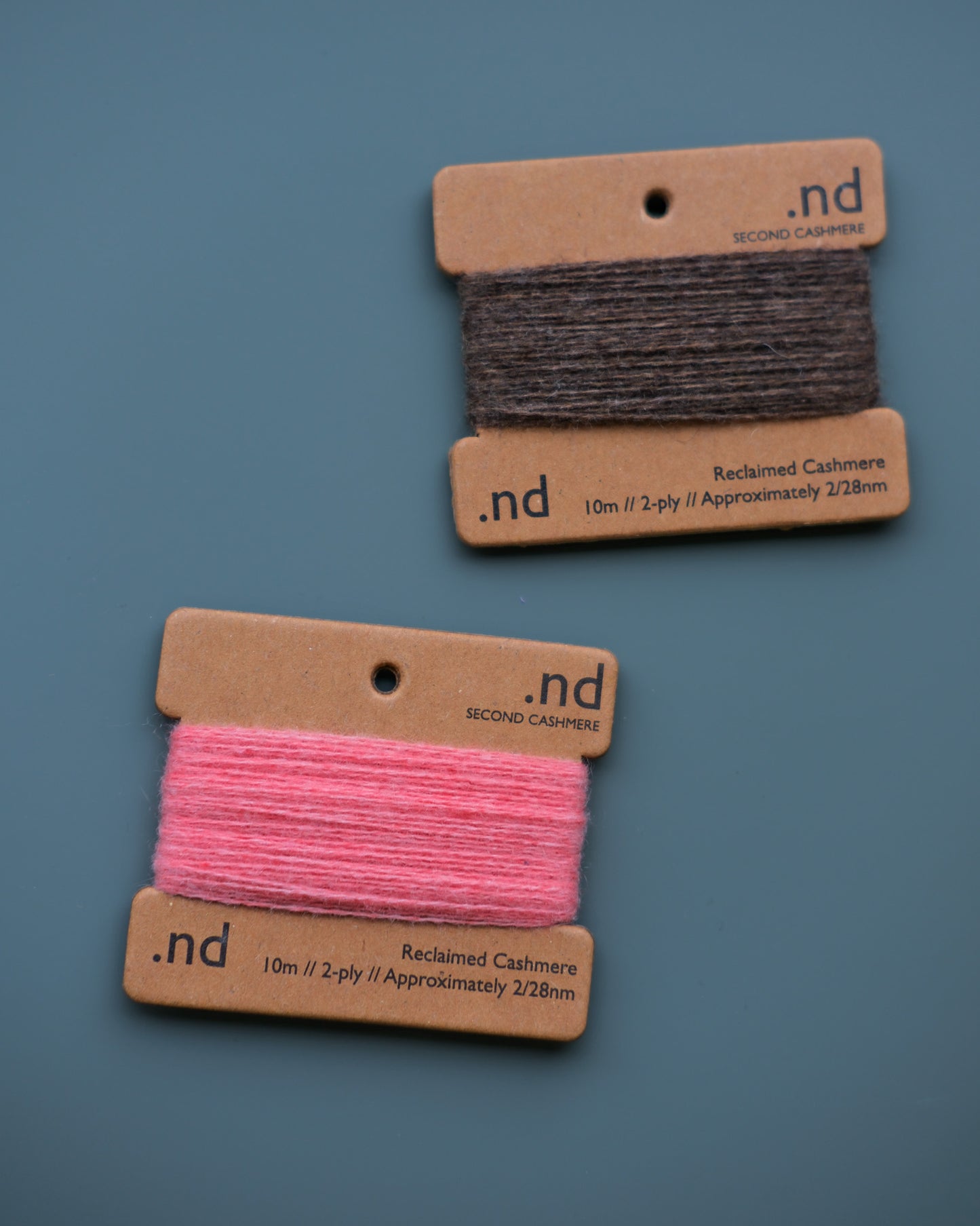 Two spools of cashmere thread, one pink and one brown, on cardboard holders with 'nd' branding against a blue background.