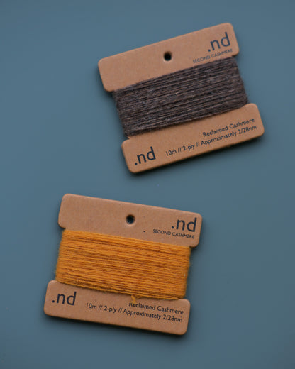 Two spools of reclaimed cashmere on cardboard cards with 'nd' branding against a blue background