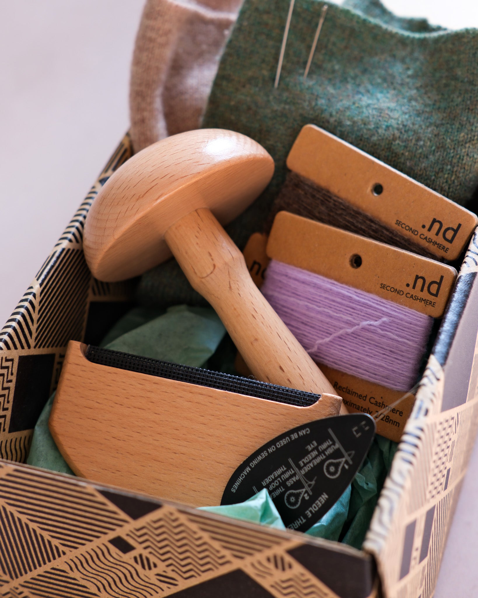 Cashmere mending kit containing a wooden darning mushroom, cashmere practice swatches, a wool comb, and cashmere mending wool
