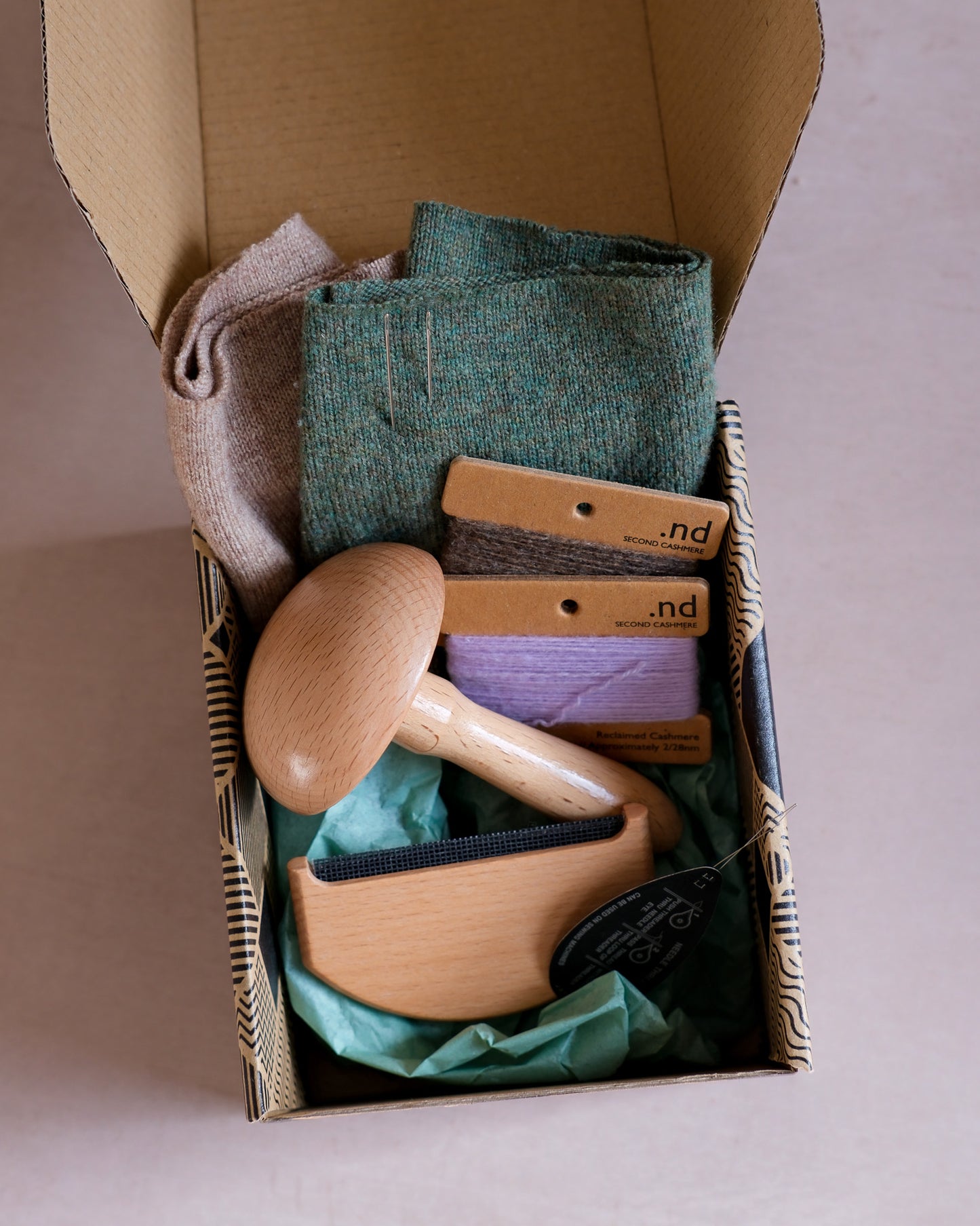 Cashmere mending kit containing a wooden darning mushroom, cashmere practice swatches, a wool comb, and cashmere mending wool