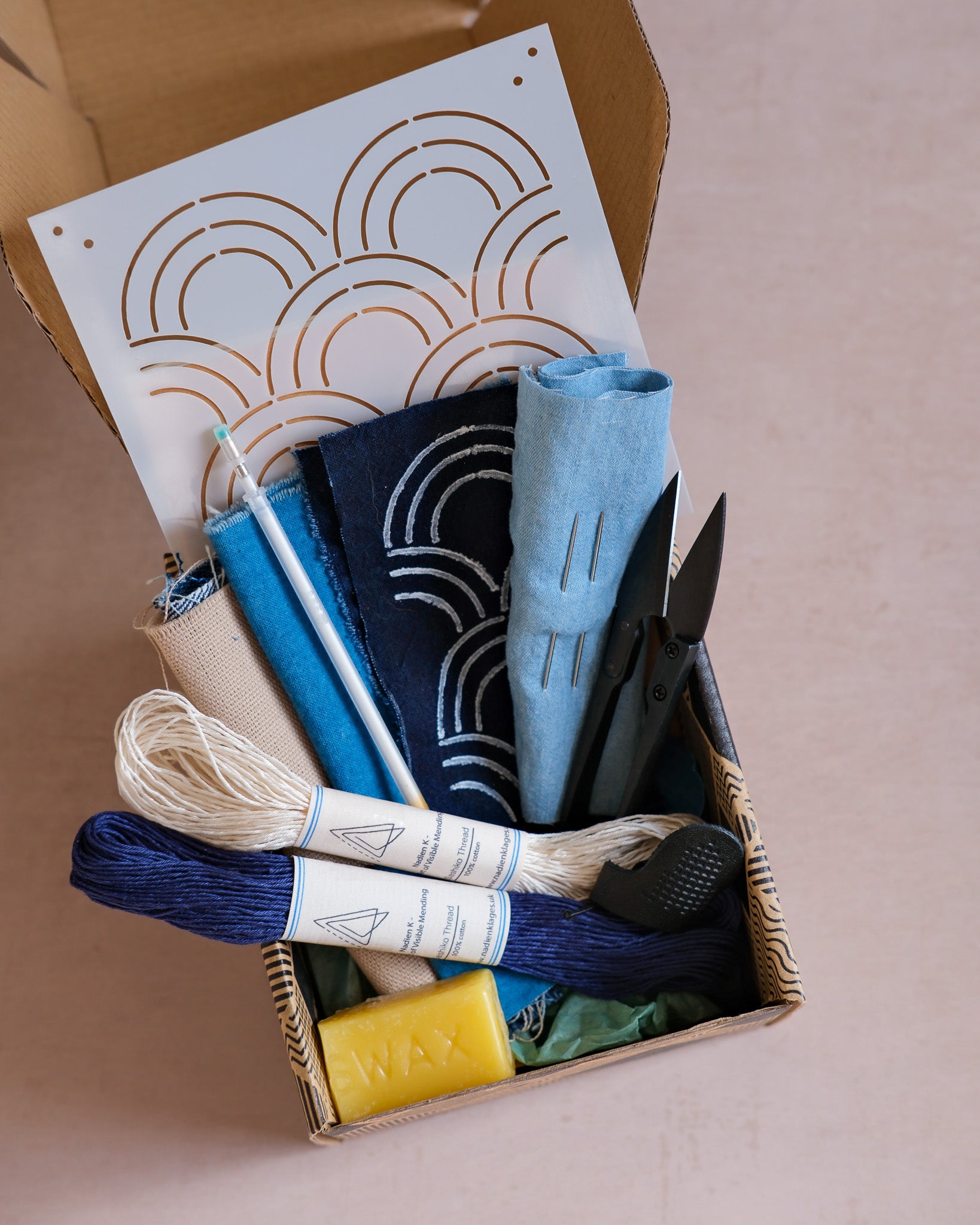 Denim sashiko repair kit including beeswax, a chalk pen, sashiko thread in blue and white, a sashiko stencil, two sashiko needles, a leather thimble and nickel free snips