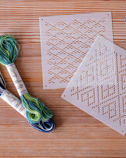 Two skeins of Sashiko embroidery floss in blue and green gradient colors, two white stencil patterns 