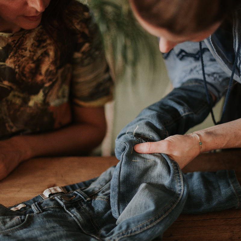 Two people examining a pair of blue jeans in an upcycling workshop on a wooden table.