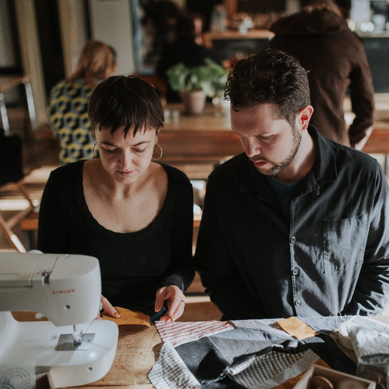 Two people working on a sewing project at a table with a sewing machine.