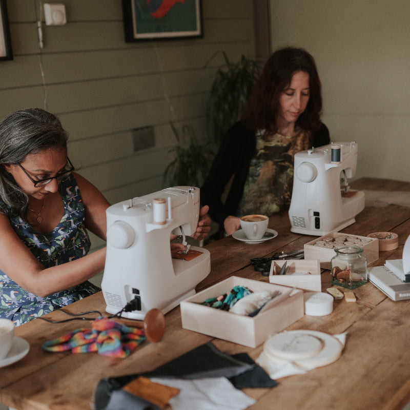 Three women working on sewing machines at a wooden table for a mending and upcycling workshop