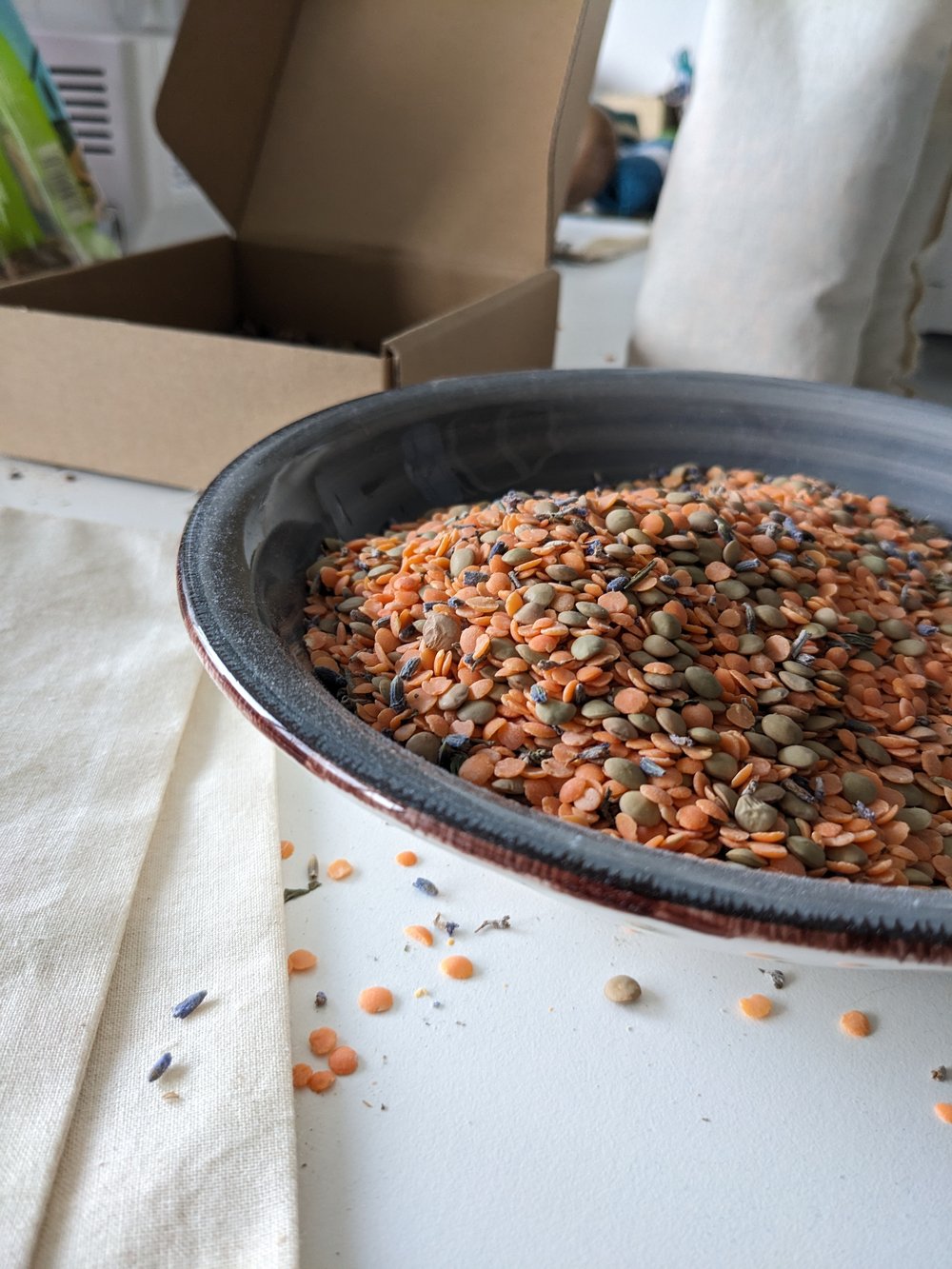 Black bowl filled with multicolored lentils on a white surface with a cardboard box in the background.